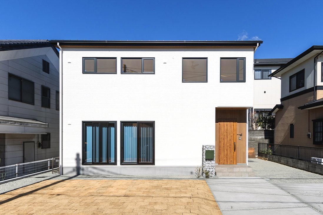 白い塗り壁調の外壁にブラックのフレームと木目がアクセントの外観