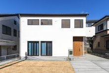 白い塗り壁調の外壁にブラックのフレームと木目がアクセントの外観